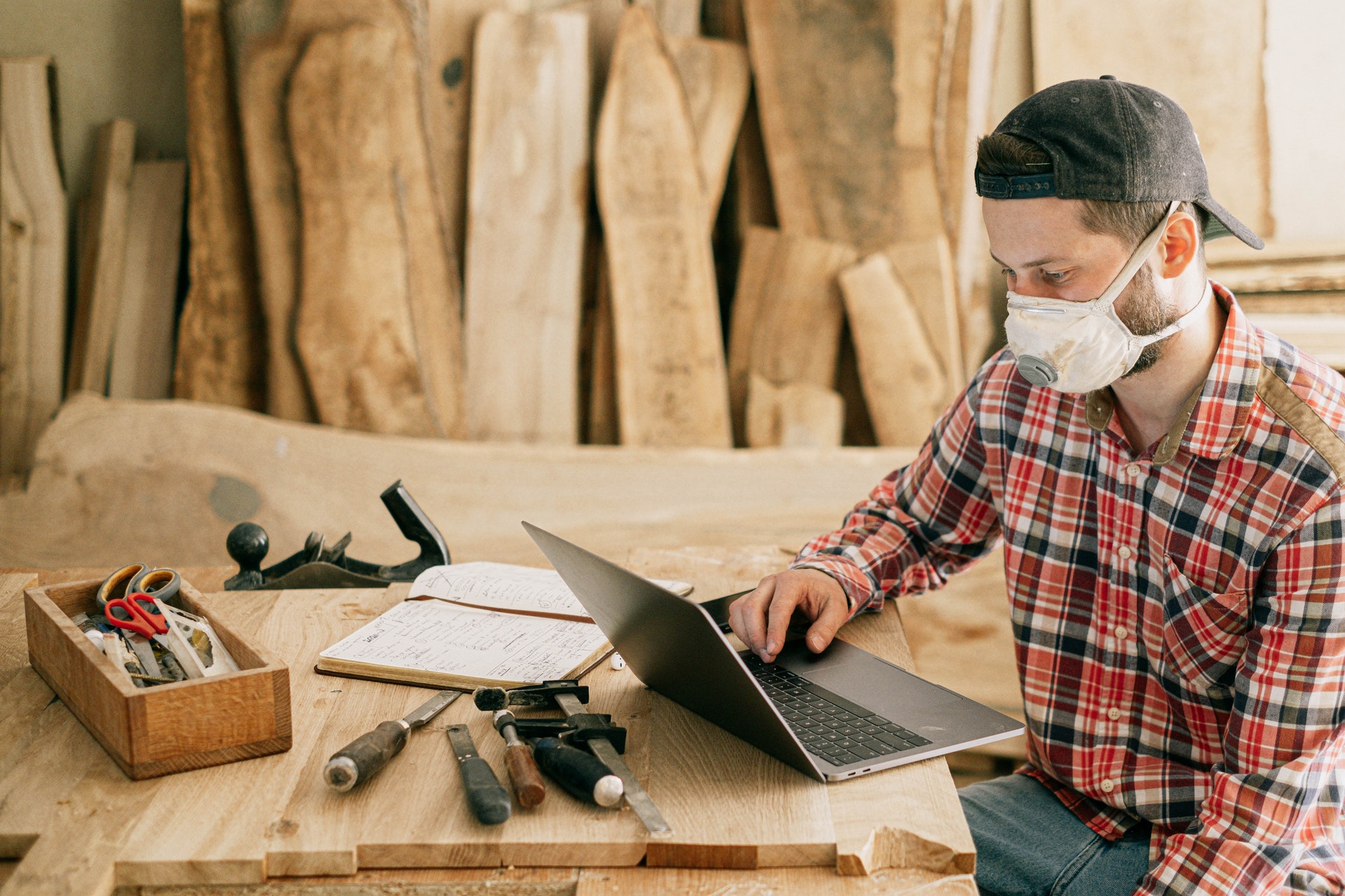 Handwerker sitzt in seinem Betrieb an einer Werkbank, während er ein Laptop benutzz